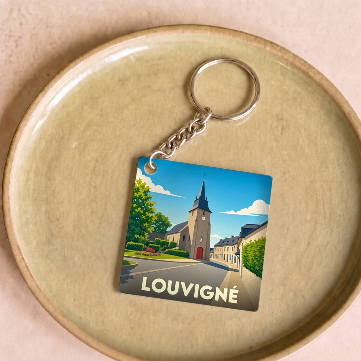 Porte-clés souvenir de la ville de Louvigné avec une illustration stylisée d'une église sous un ciel bleu.
