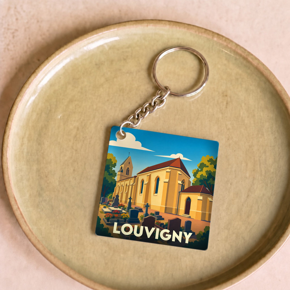 Porte-clés souvenir de la ville de Louvigny avec une illustration stylisée de son église et de son cimetière.