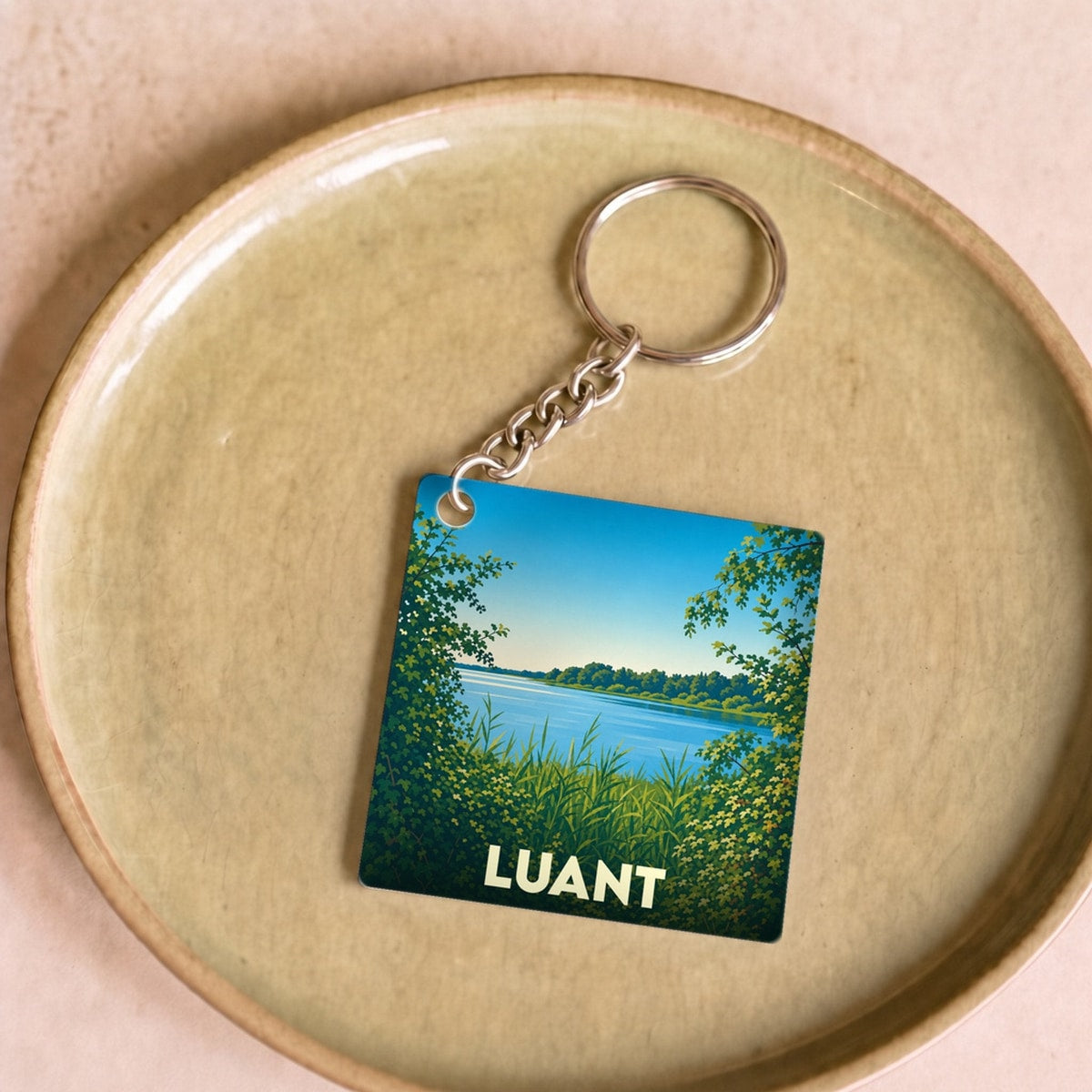 Porte-clés souvenir de la ville de Luant avec une illustration stylisée d'un paysage de lac bordé de verdure.