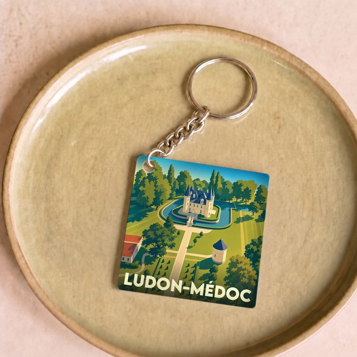Porte-clés souvenir de la ville de Ludon-Médoc avec une illustration stylisée d'un château entouré de jardins.