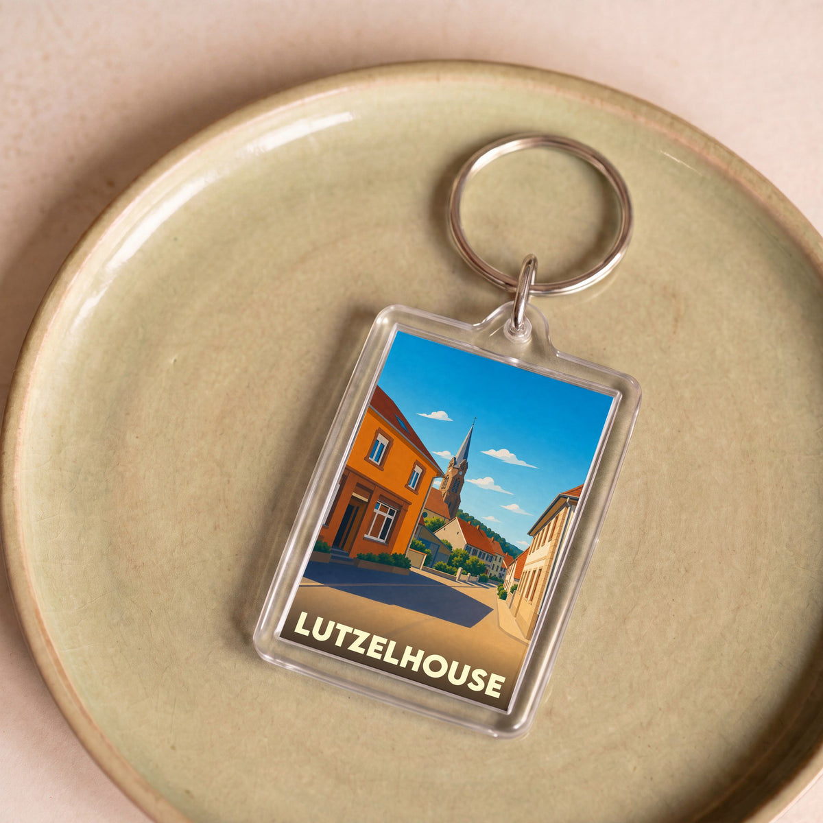 Porte-clés souvenir de la ville de Lutzelhouse avec une illustration stylisée d'une rue pittoresque.
