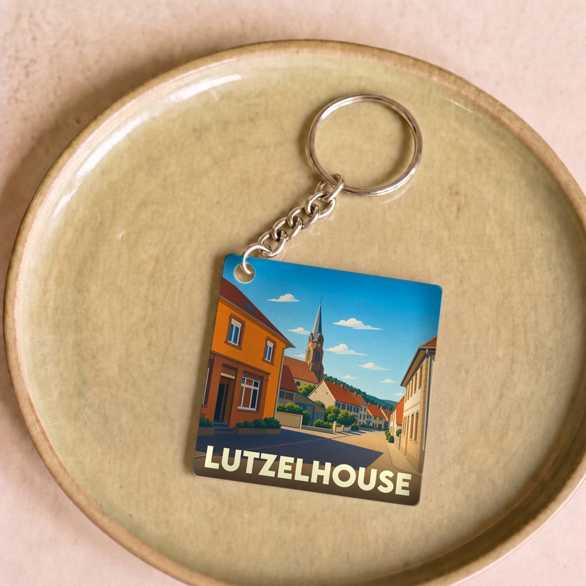 Porte-clés souvenir de la ville de Lutzelhouse avec une illustration stylisée d'une rue pittoresque.