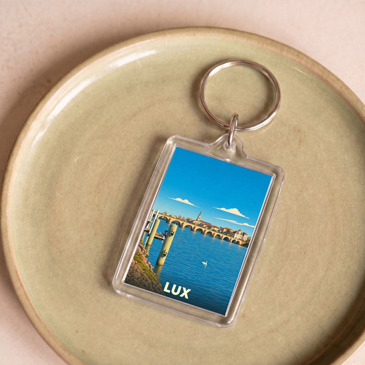 Porte-clés souvenir de la ville de Lux avec une illustration stylisée d'un paysage urbain au bord de l'eau.