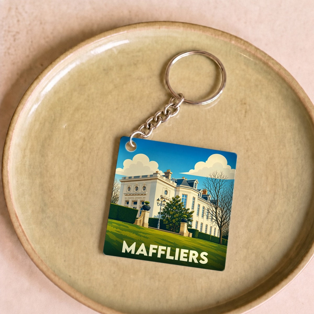 Porte-clés souvenir de la ville de Maffliers avec une illustration stylisée d'un château sous un ciel bleu.
