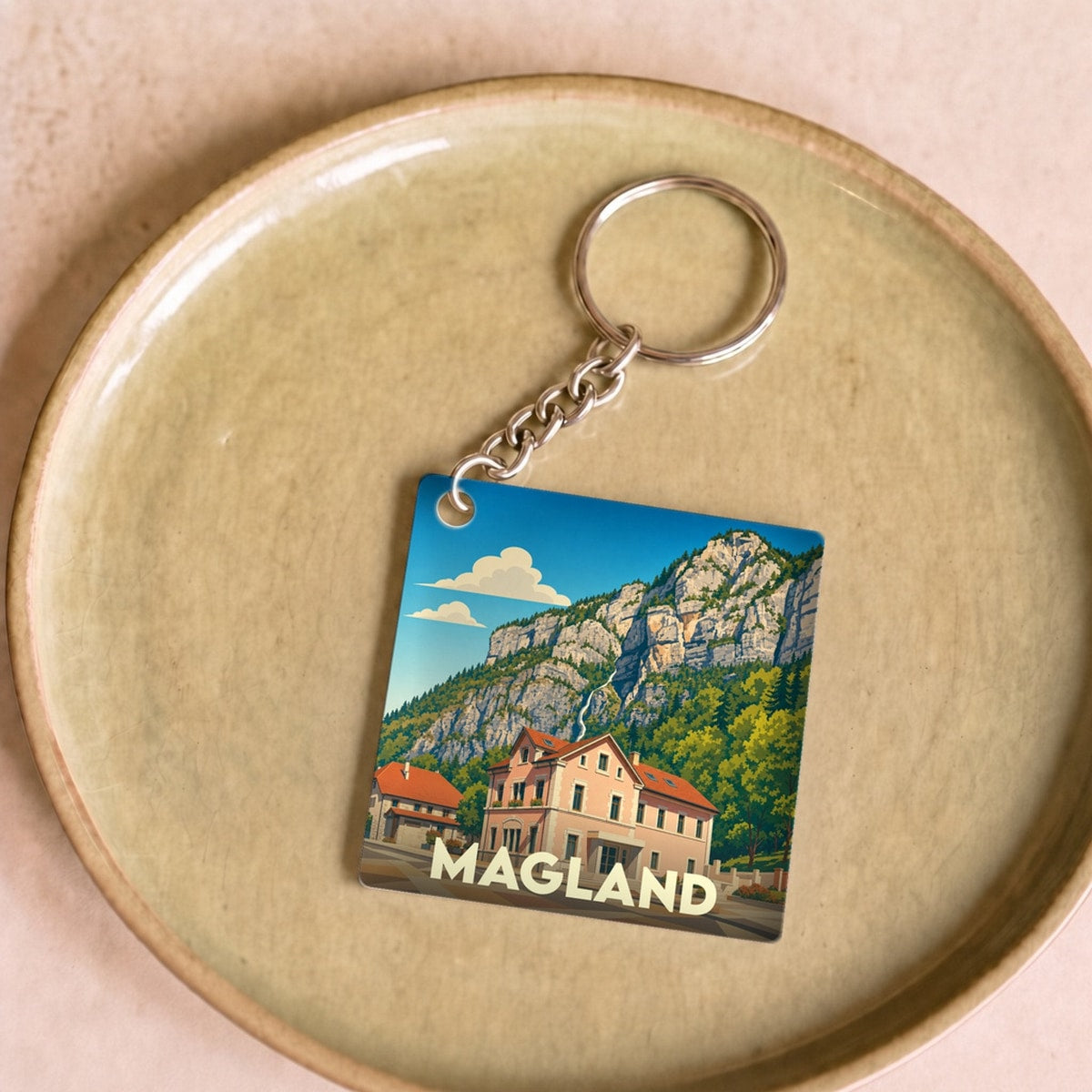 Porte-clés souvenir de la ville de Magland avec une illustration stylisée d'un paysage montagneux.