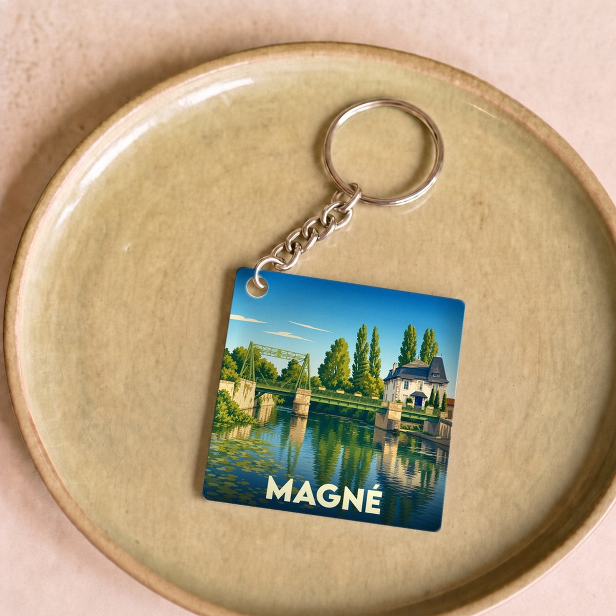 Porte-clés souvenir de la ville de Magné avec une illustration stylisée d'un pont et de reflets sur l'eau.