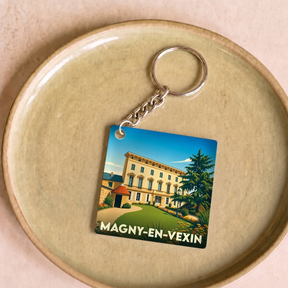 Porte-clés souvenir de la ville de Magny-en-Vexin avec une illustration stylisée d'un manoir et de son jardin.