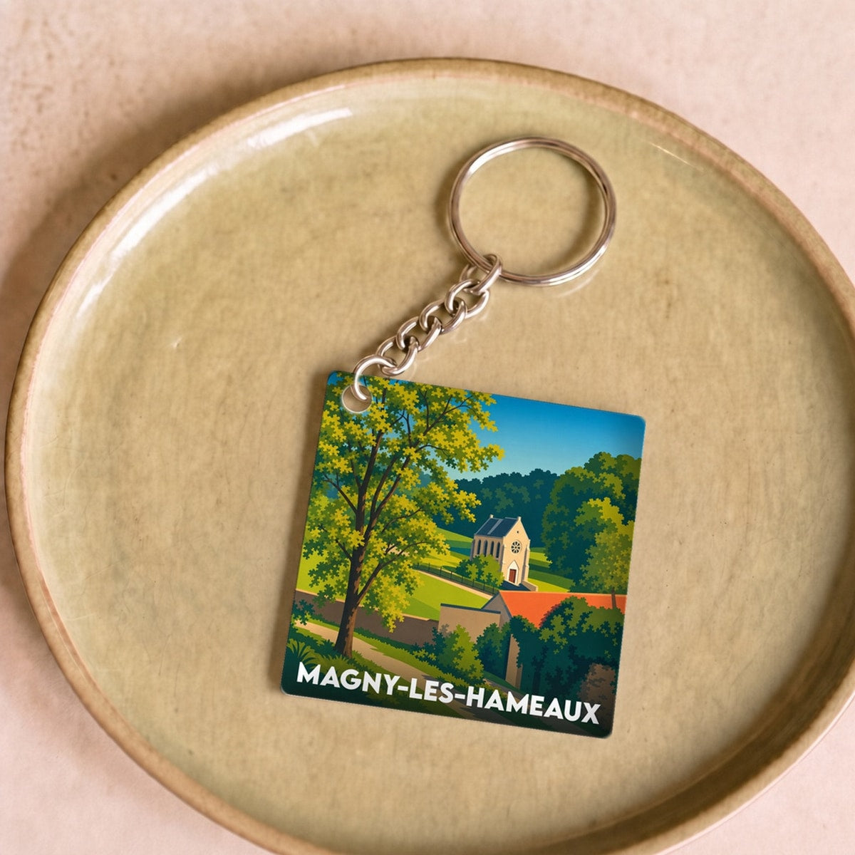 Porte-clés souvenir de la ville de Magny-les-Hameaux avec une illustration paysagère stylisée.