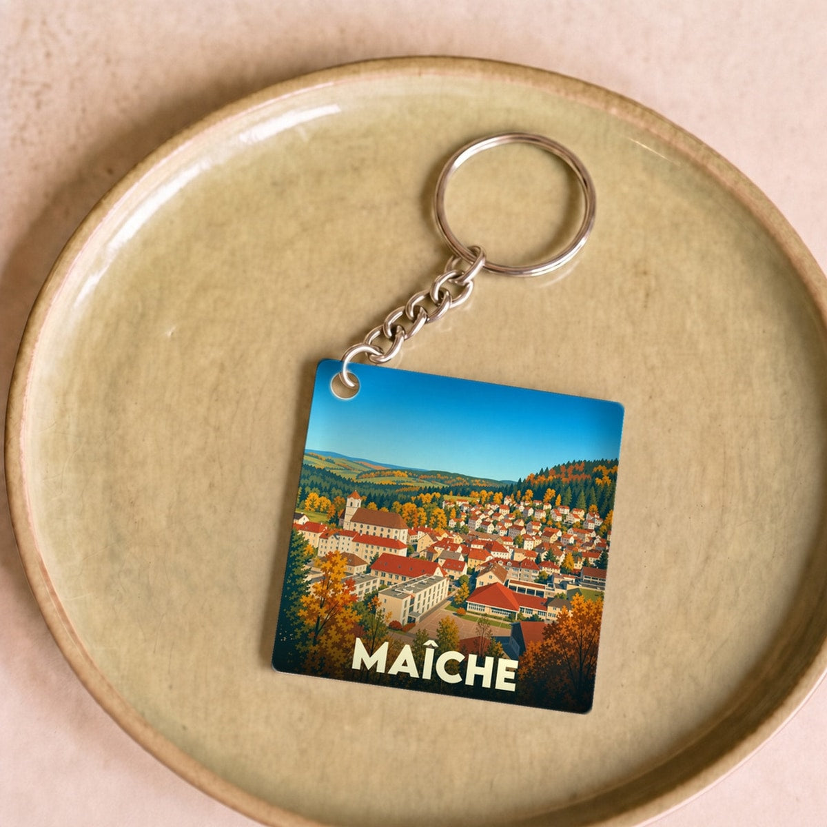 Porte-clés souvenir de la ville de Maîche avec une illustration stylisée de son paysage urbain en automne.