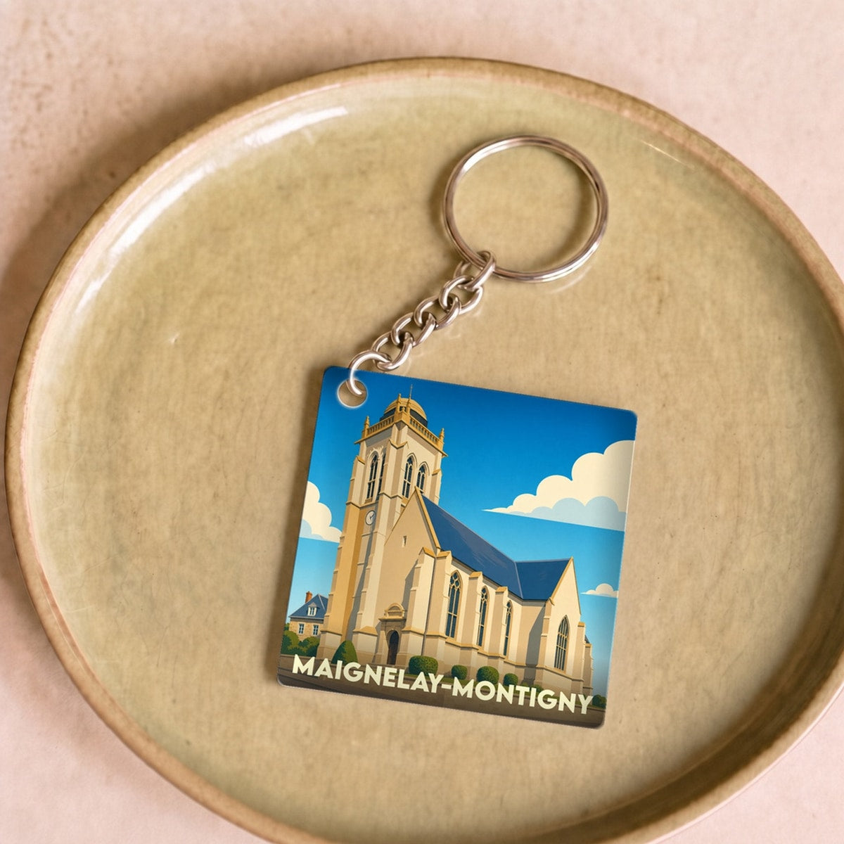 Porte-clés souvenir de Maignelay-Montigny illustré par un dessin stylisé de son église sous un ciel bleu.