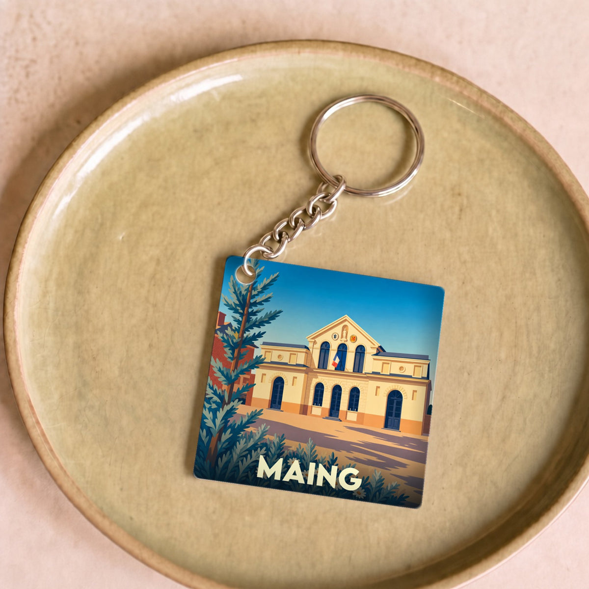 Porte-clés souvenir de la ville de Maing avec une illustration stylisée de sa mairie.