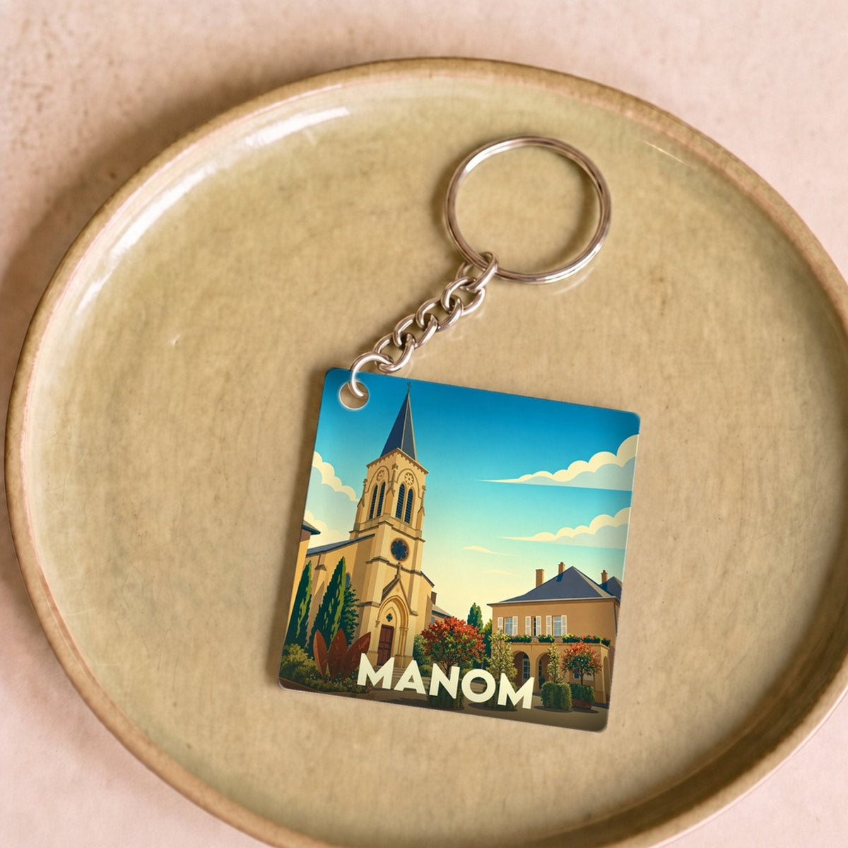 Porte-clés souvenir de la ville de Manom avec une illustration stylisée.