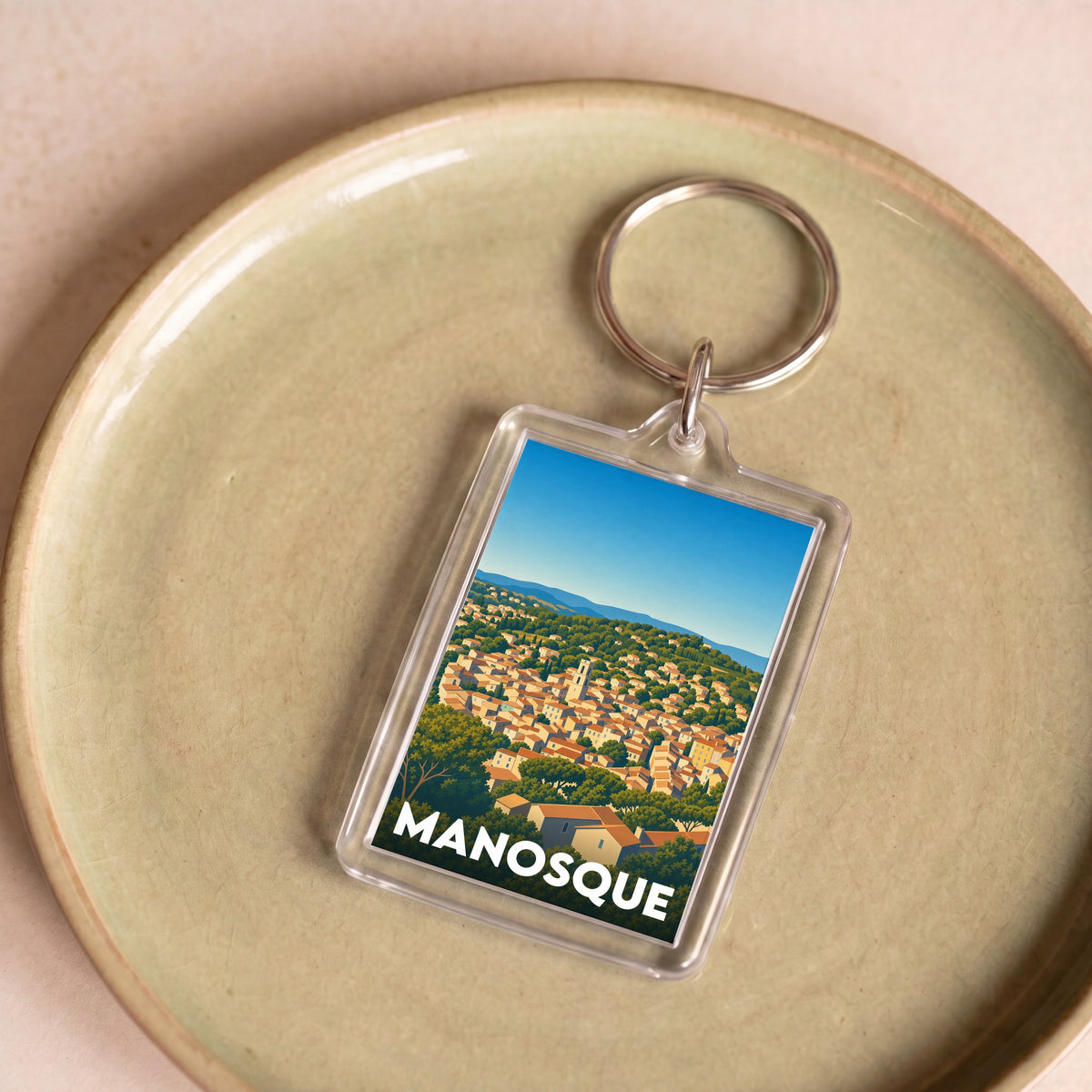 Porte-clés souvenir de la ville de Manosque avec une illustration stylisée.