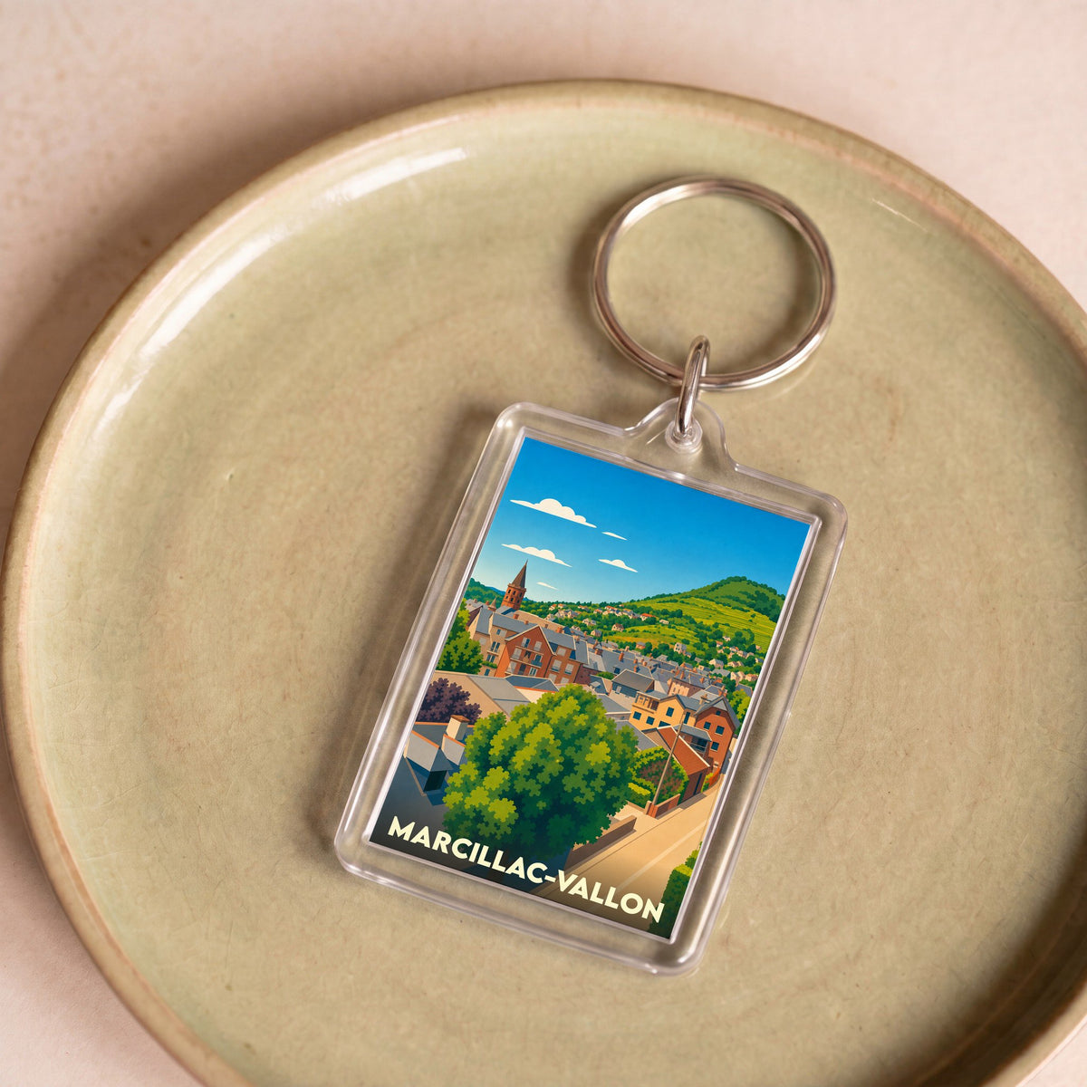 Porte-clés souvenir de la ville de Marcillac-Vallon avec une illustration stylisée d'un paysage urbain.