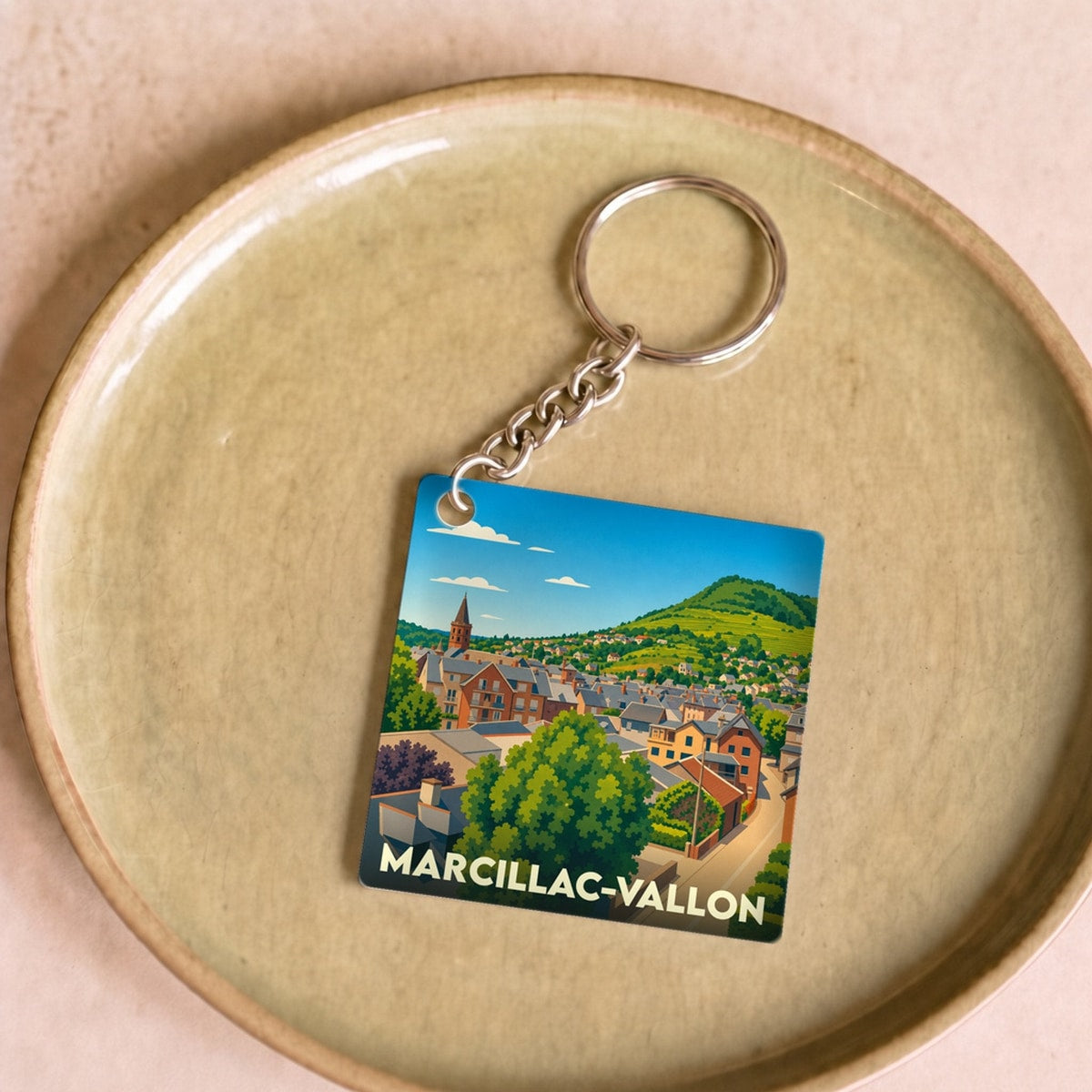 Porte-clés souvenir de Marcillac-Vallon illustré d'un paysage urbain stylisé et coloré.
