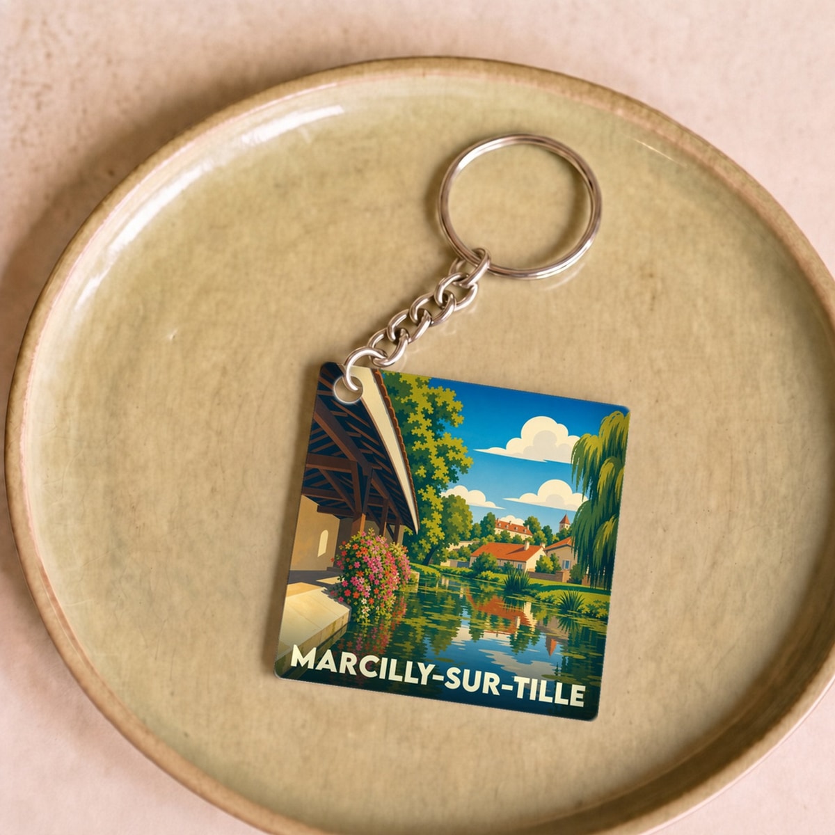 Porte-clés souvenir de Marcilly-sur-Tille avec une illustration colorée et stylisée de la ville au bord de l'eau.