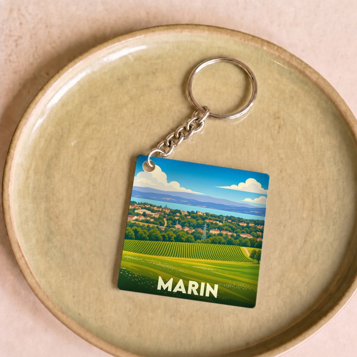 Porte-clés souvenir de la ville de Marin avec une illustration stylisée de paysages vallonnés.