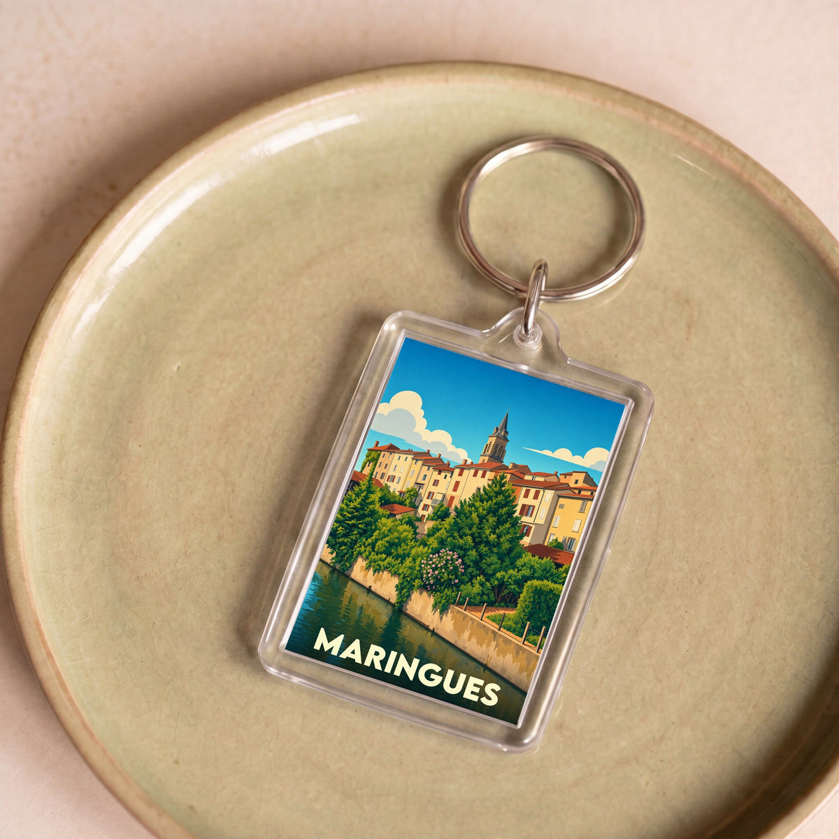 Porte-clés souvenir de la ville de Maringues avec une illustration stylisée d'un paysage urbain au bord de l'eau.