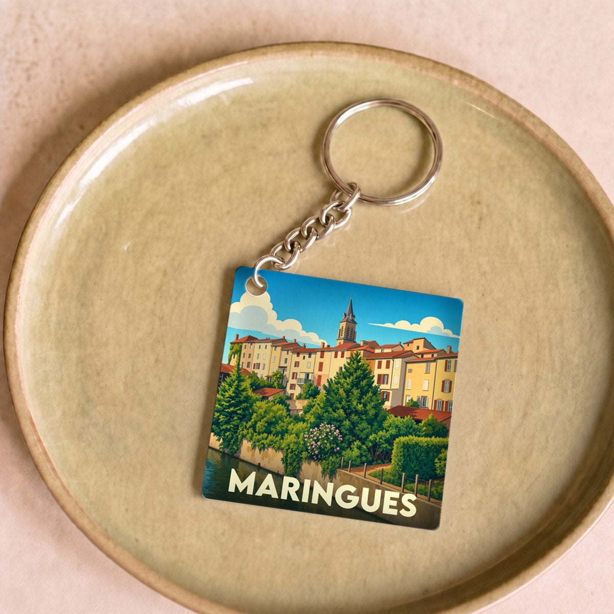 Porte-clés souvenir de la ville de Maringues avec une illustration stylisée d'un paysage urbain au bord de l'eau.