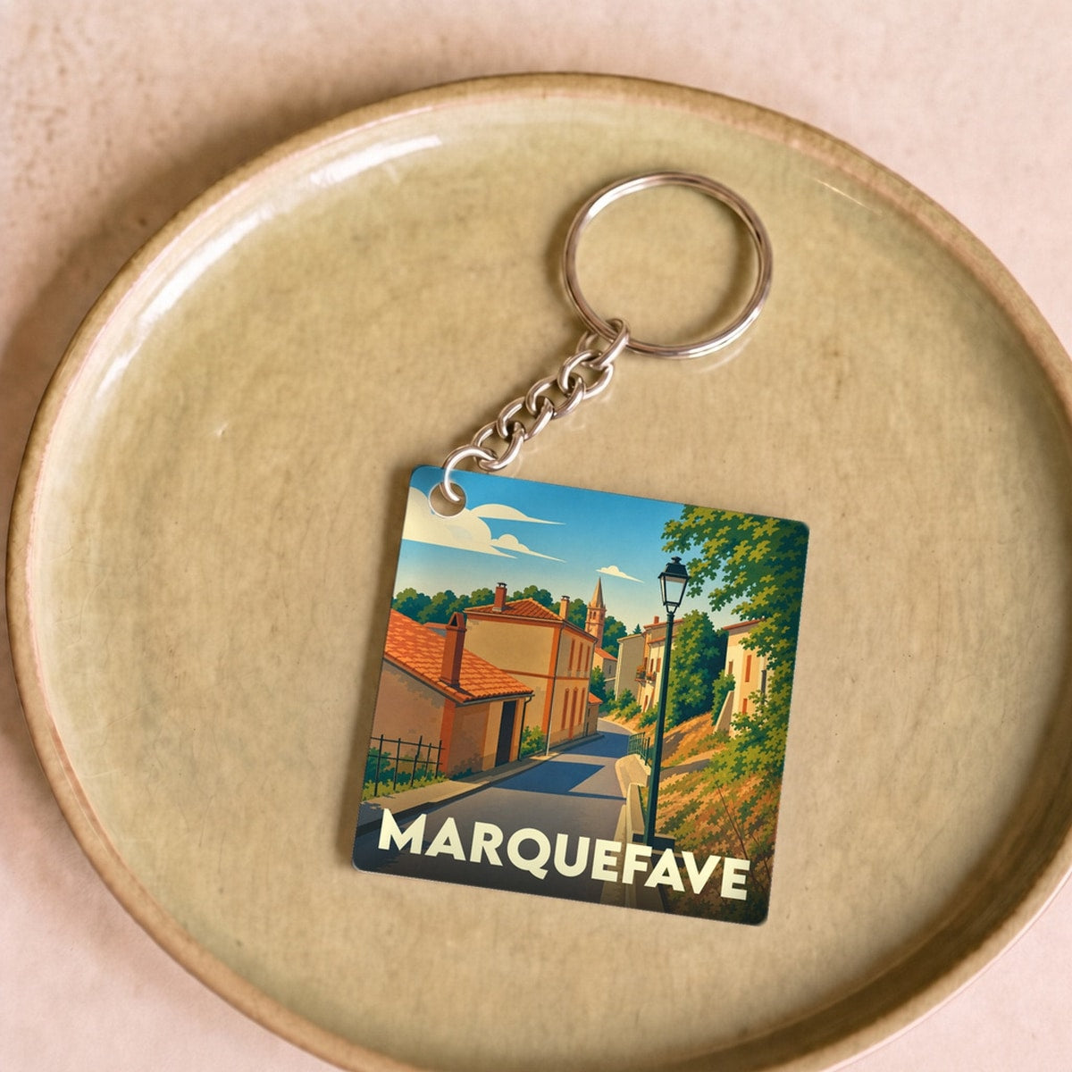 Porte-clés souvenir de la ville de Marquefave avec une illustration stylisée d'une rue ensoleillée.