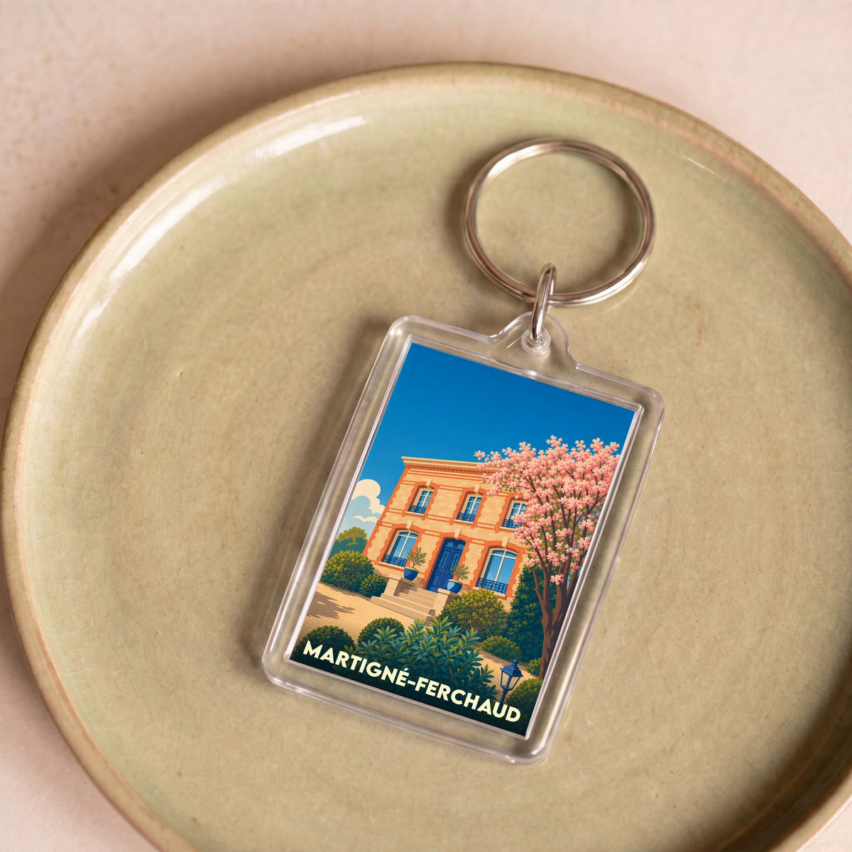 Porte-clés souvenir de Martigné-Ferchaud avec une illustration stylisée d'une maison bourgeoise et d'un arbre en fleurs.