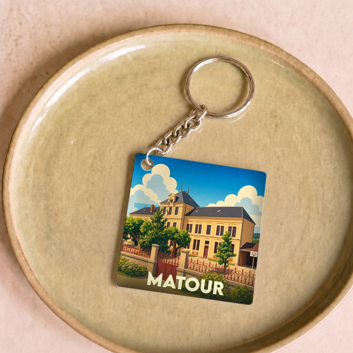 Porte-clés souvenir de la ville de Matour avec une illustration stylisée d'un bâtiment historique sous un ciel bleu.