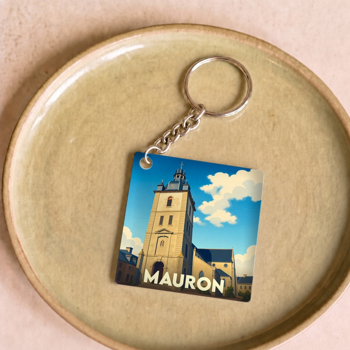 Porte-clés souvenir de la ville de Mauron avec une illustration stylisée de son église sous un ciel bleu.