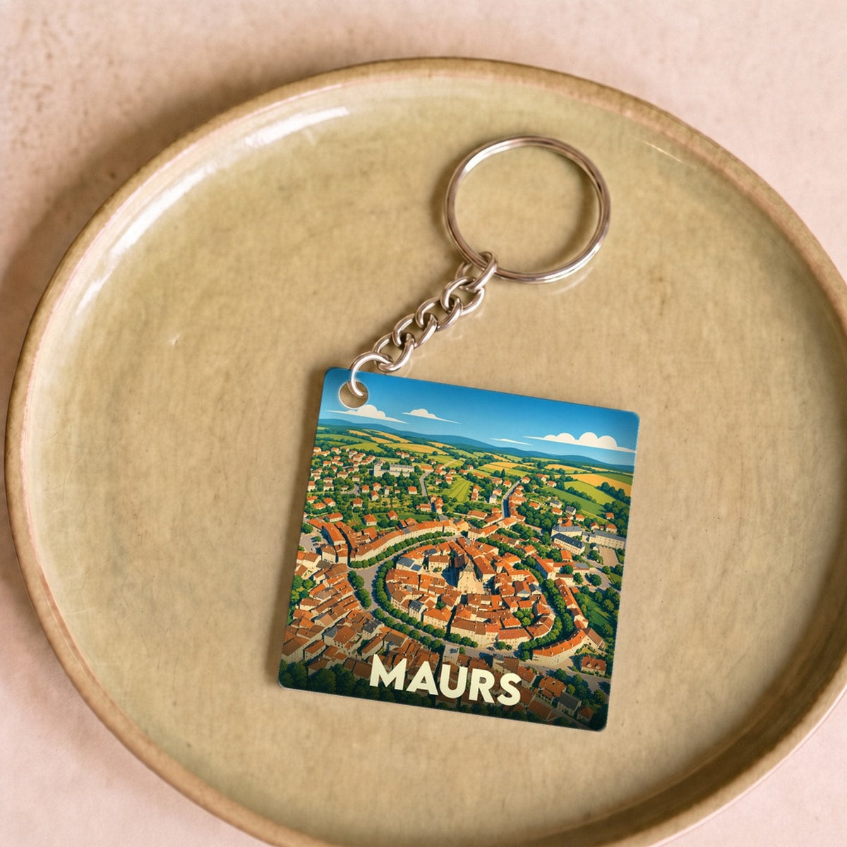 Porte-clés souvenir de la ville de Maurs avec une illustration stylisée vue du ciel.