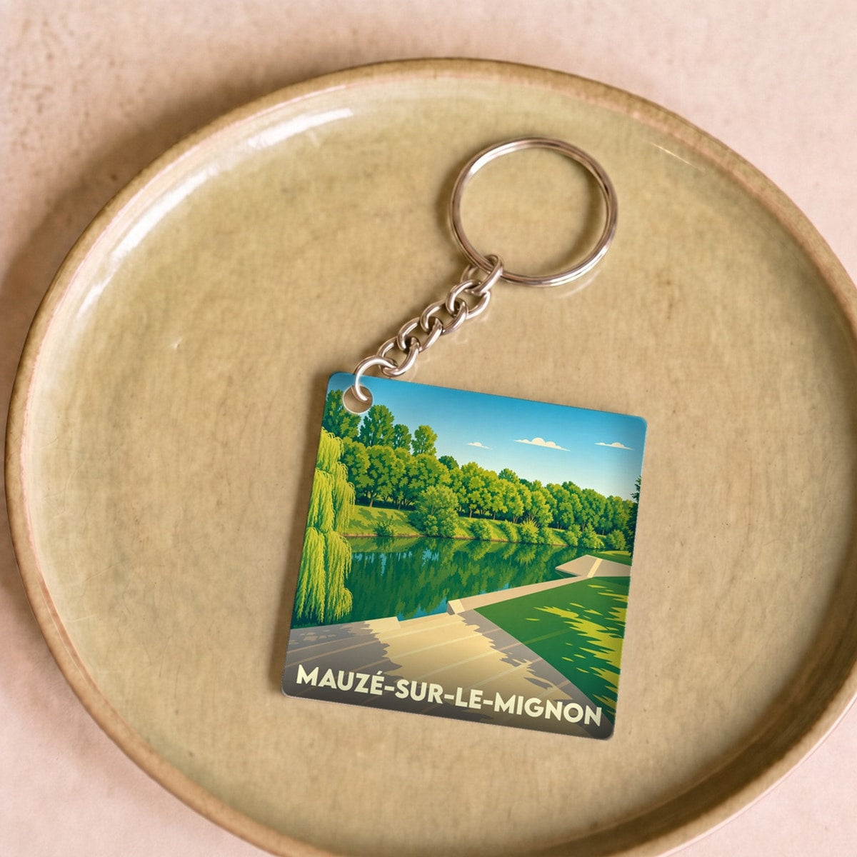 Porte-clés souvenir de la ville de Mauzé-sur-le-Mignon avec une illustration stylisée d'un bord de rivière.