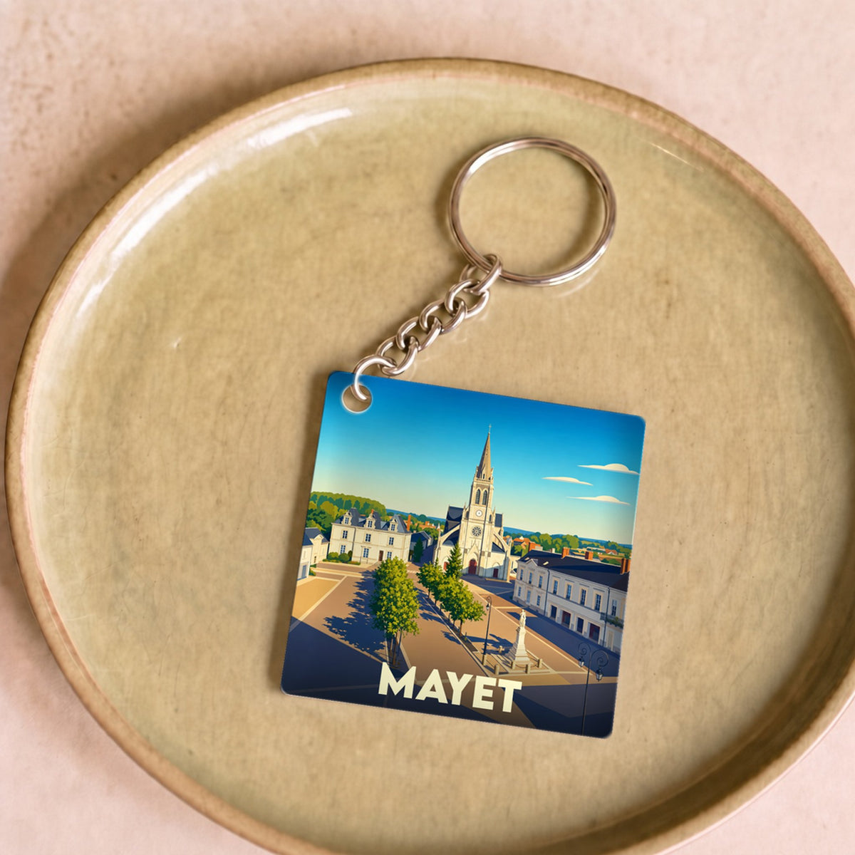 Porte-clés souvenir de la ville de Mayet avec une illustration stylisée d'une place ensoleillée.