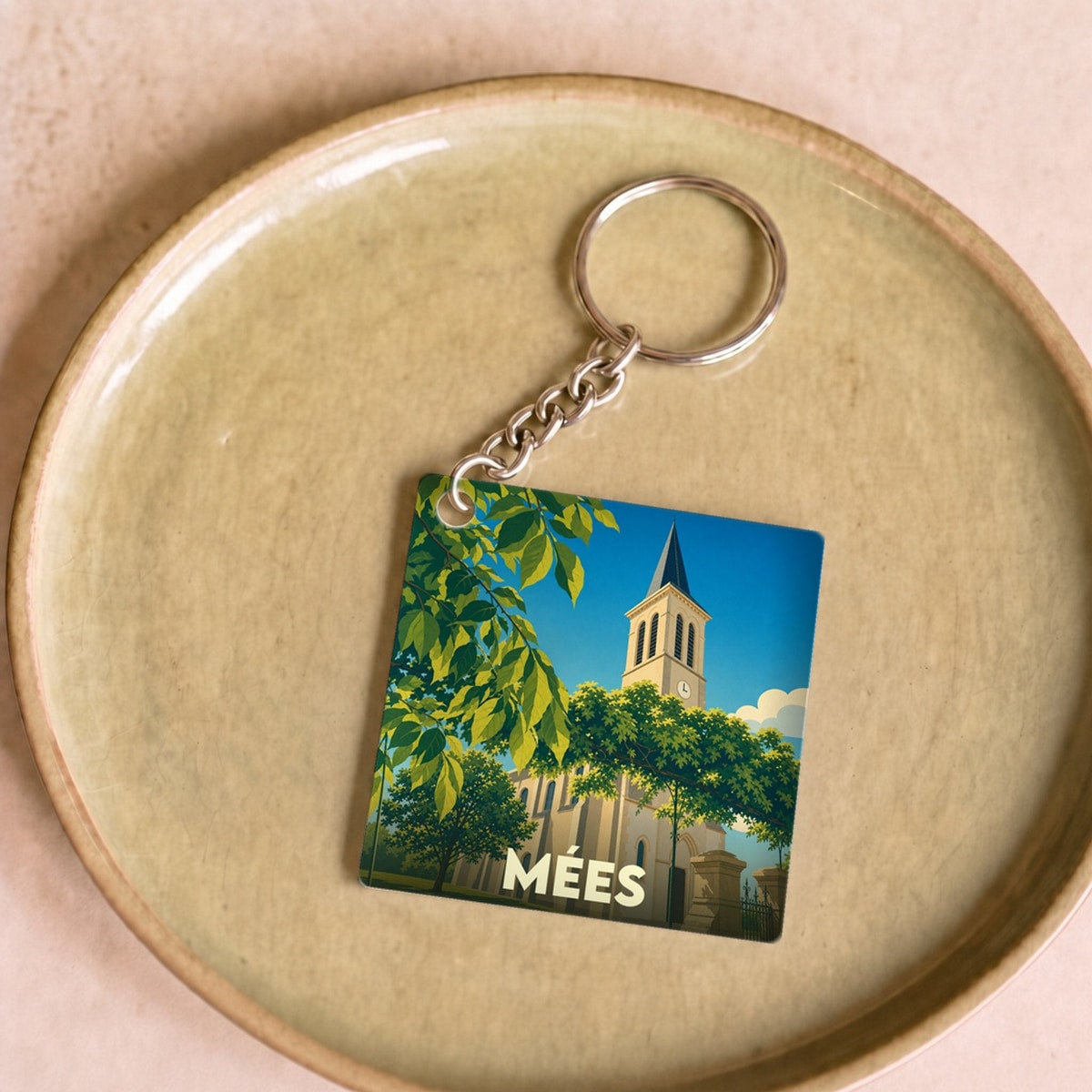 Porte-clés souvenir de la ville de Mées avec une illustration stylisée d'une église sous un ciel bleu.