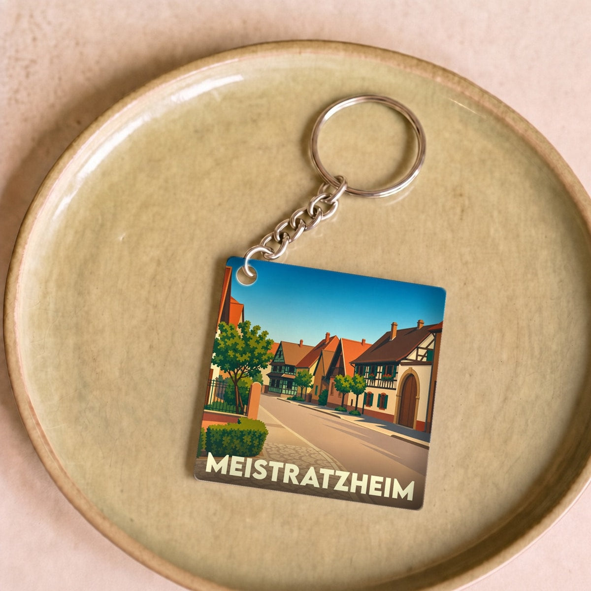 Porte-clés souvenir de la ville de Meistratzheim avec une illustration stylisée d'une rue alsacienne.