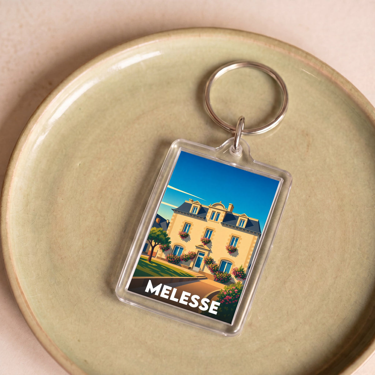 Porte-clés souvenir de la ville de Melesse avec une illustration stylisée d'un bâtiment fleuri.