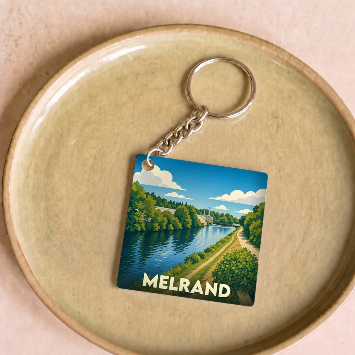 Porte-clés souvenir de la ville de Melrand avec une illustration stylisée d'un paysage de rivière.