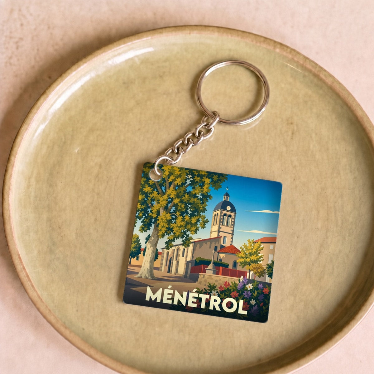 Porte-clés souvenir de la ville de Ménétrol avec une illustration stylisée d'une église et d'un platane.