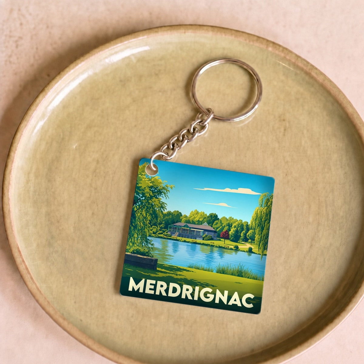Porte-clés souvenir de la ville de Merdrignac avec une illustration stylisée d'un plan d'eau.