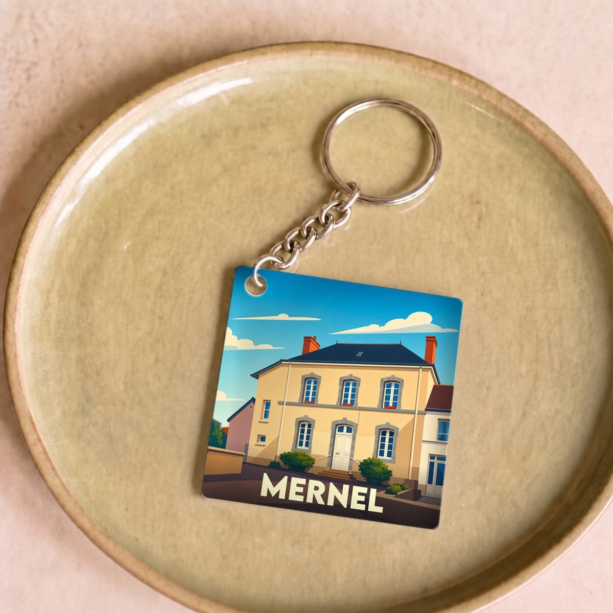 Porte-clés souvenir de la ville de Mernel avec une illustration stylisée d'un bâtiment local.