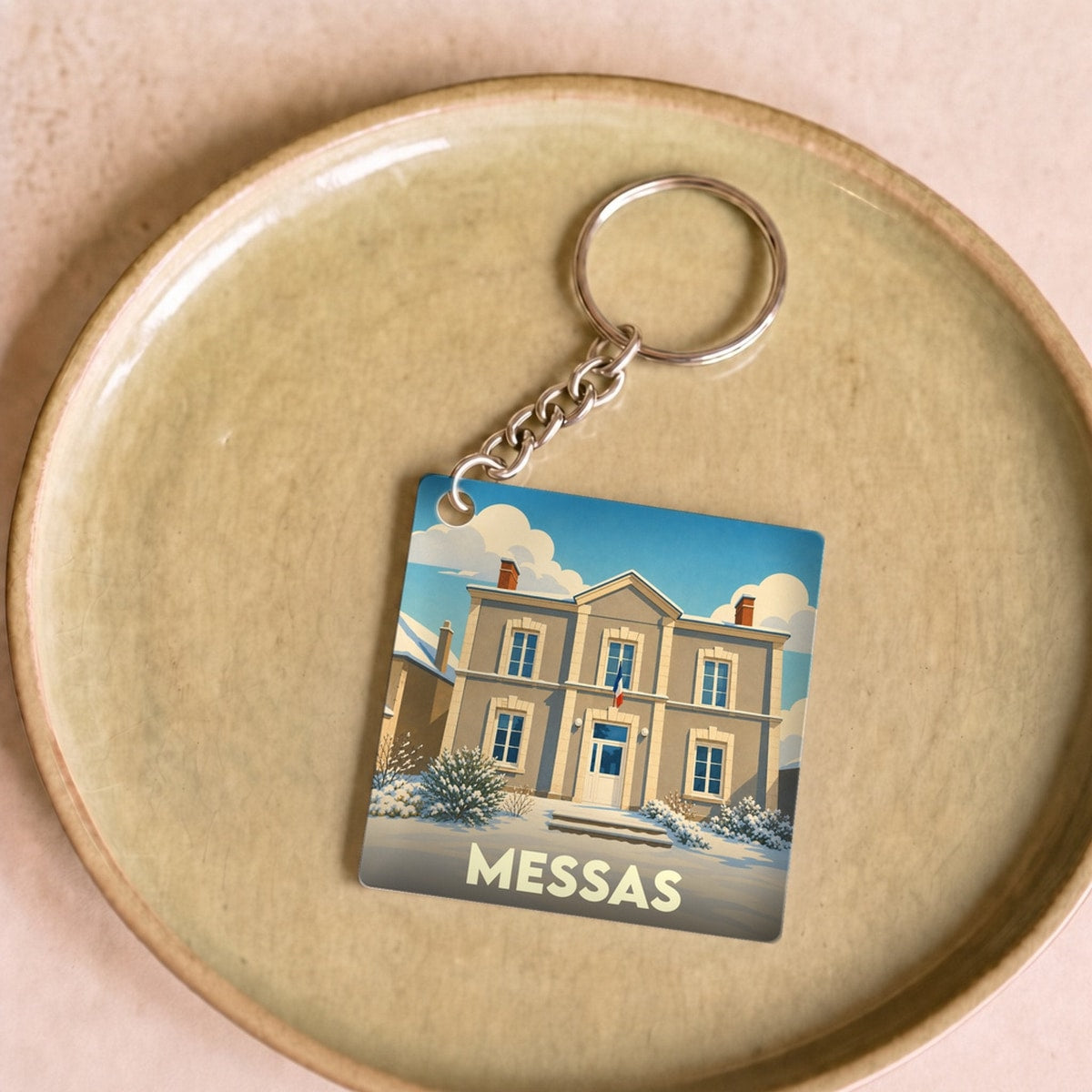 Porte-clés souvenir de la ville de Messas avec une illustration stylisée d'un bâtiment sous la neige.