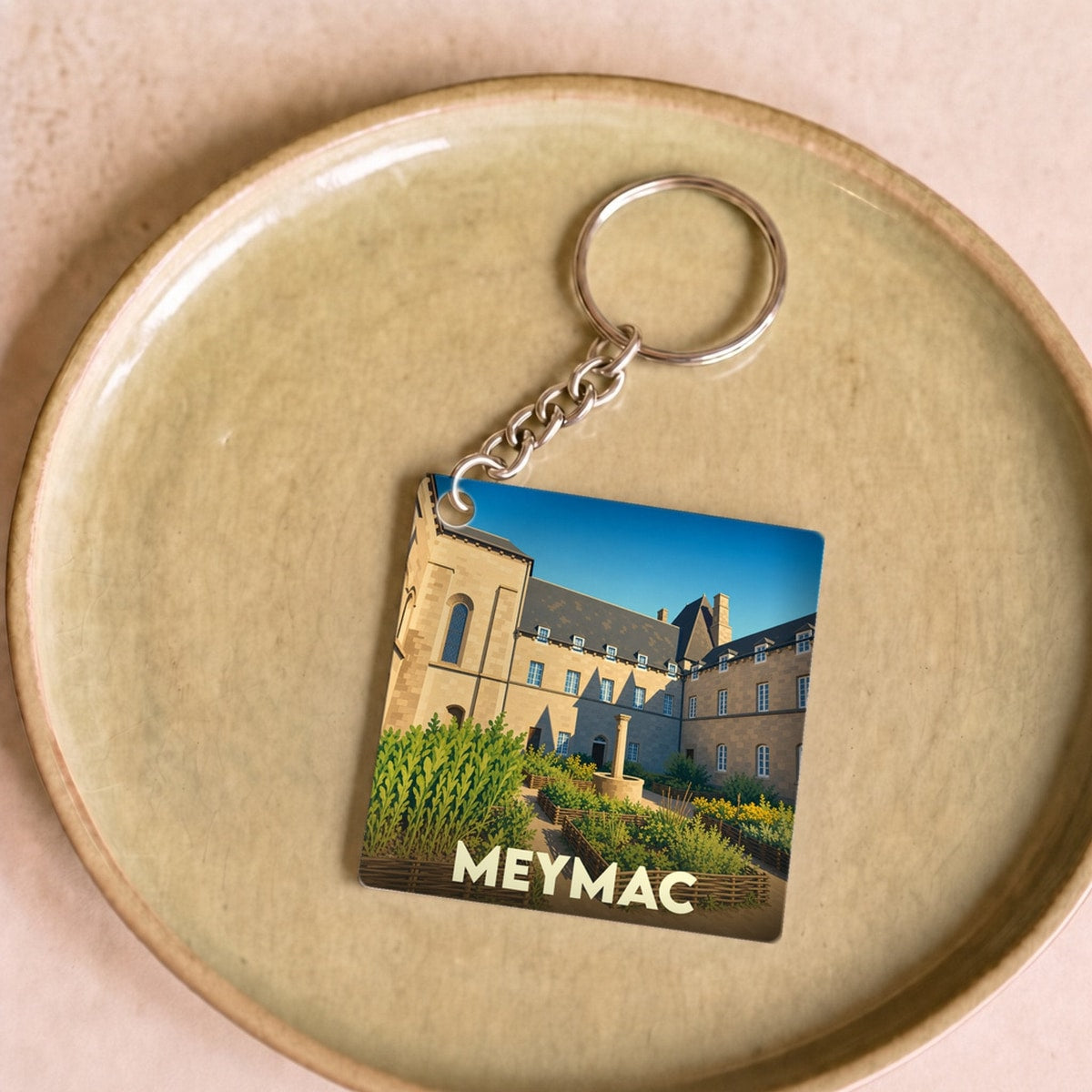 Porte-clés souvenir de la ville de Meymac avec une illustration stylisée de son abbaye et de ses jardins.