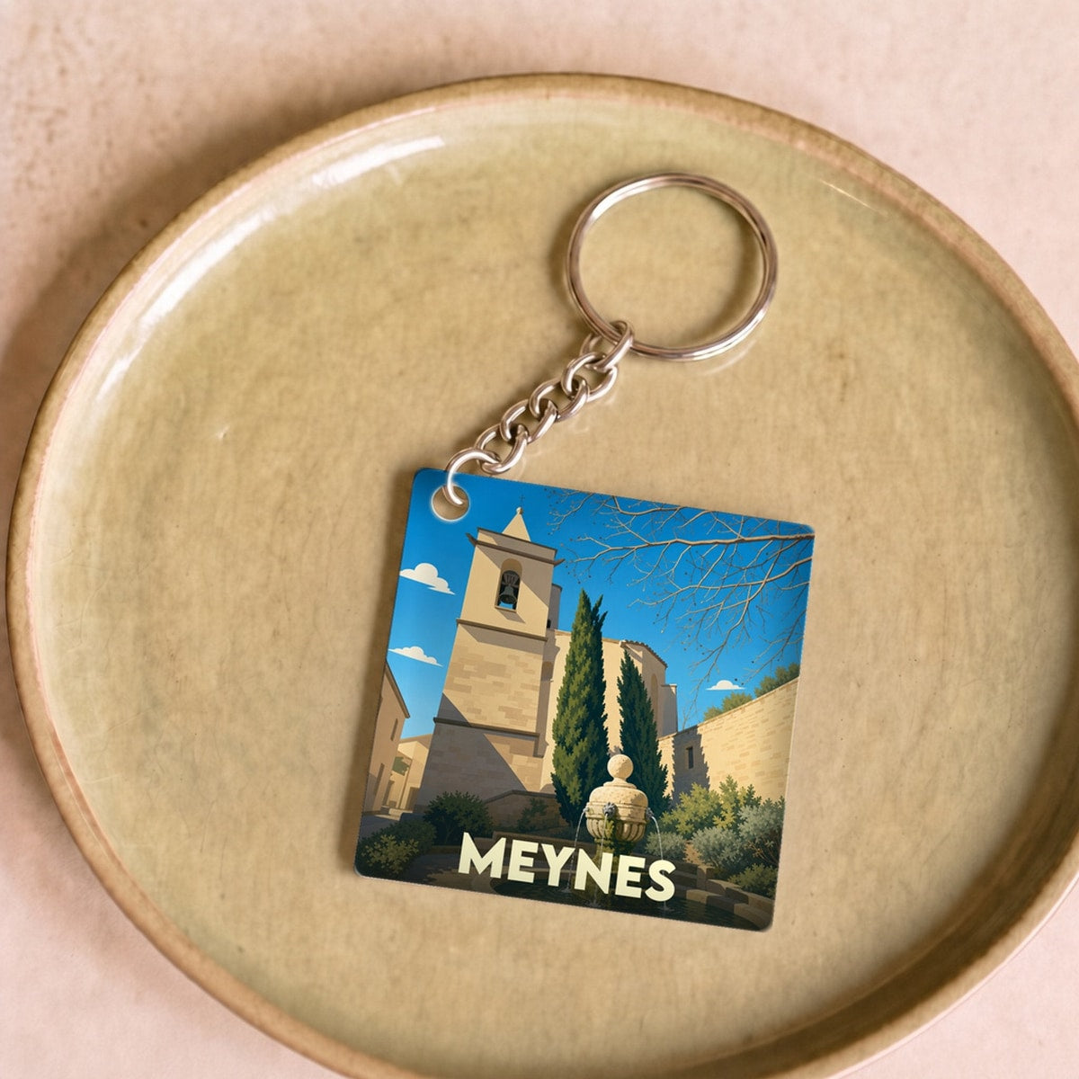 Porte-clés souvenir de la ville de Meynes avec une illustration stylisée d'une église et d'une fontaine.