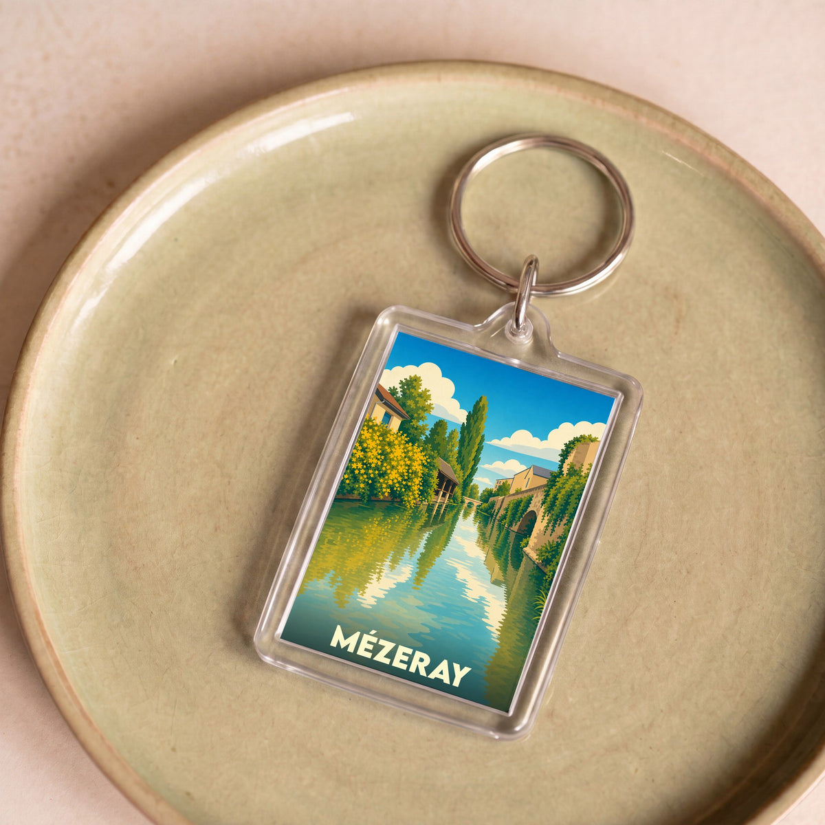 Porte-clés souvenir de la ville de Mézeray avec une illustration stylisée d'un cours d'eau bordé de verdure.