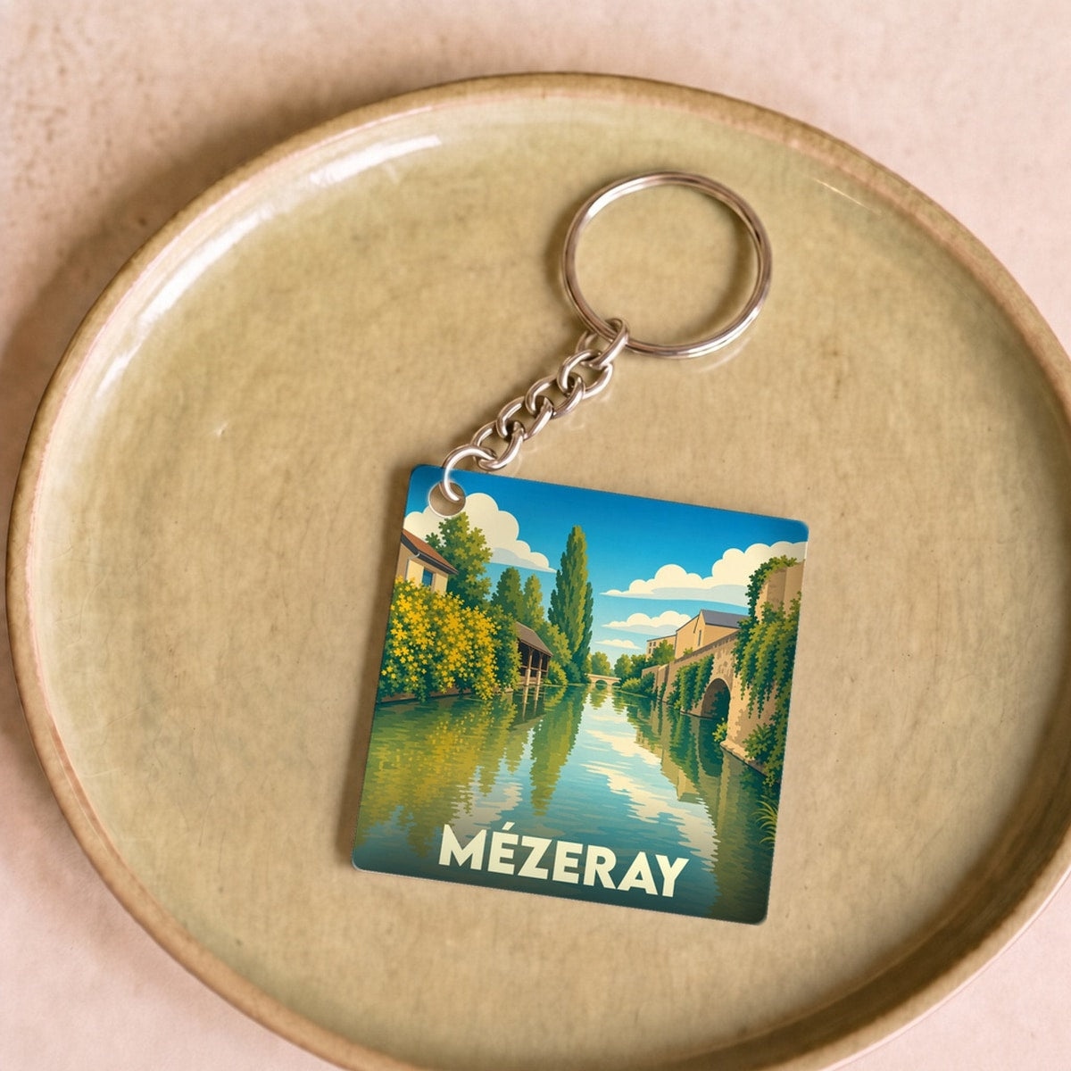 Porte-clés souvenir de la ville de Mézeray avec une illustration stylisée d'un cours d'eau bordé de verdure.
