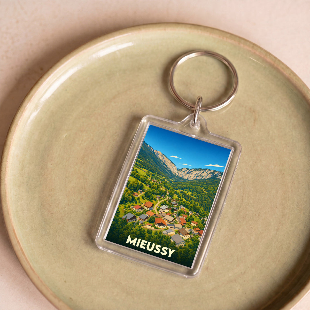 Porte-clés souvenir de la ville de Mieussy avec une illustration stylisée d'un village de montagne.