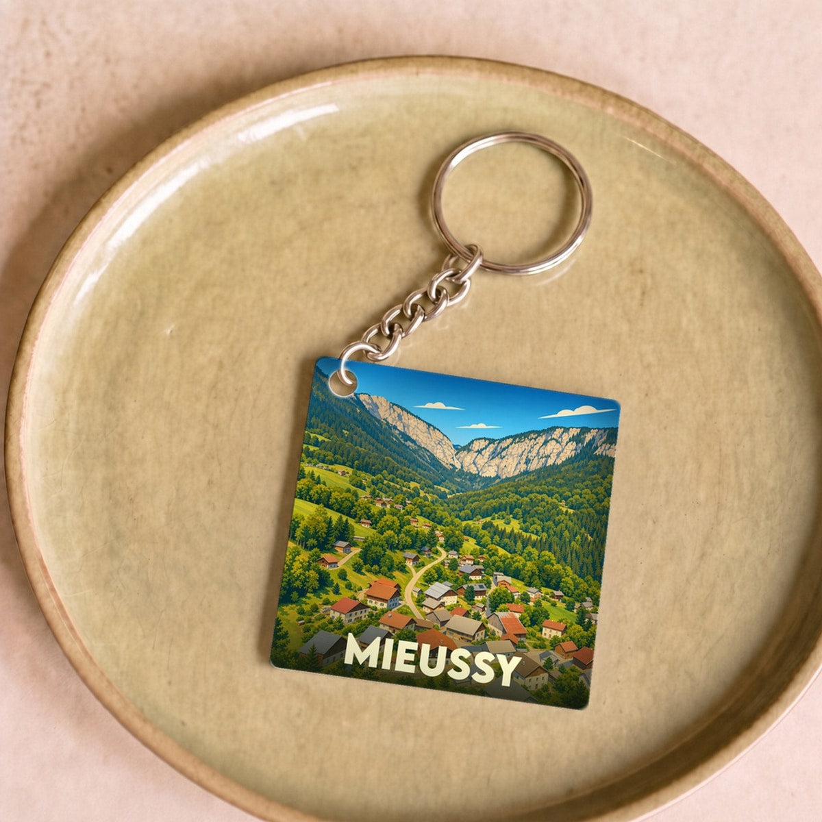 Porte-clés souvenir de la ville de Mieussy avec une illustration stylisée d'un village de montagne.