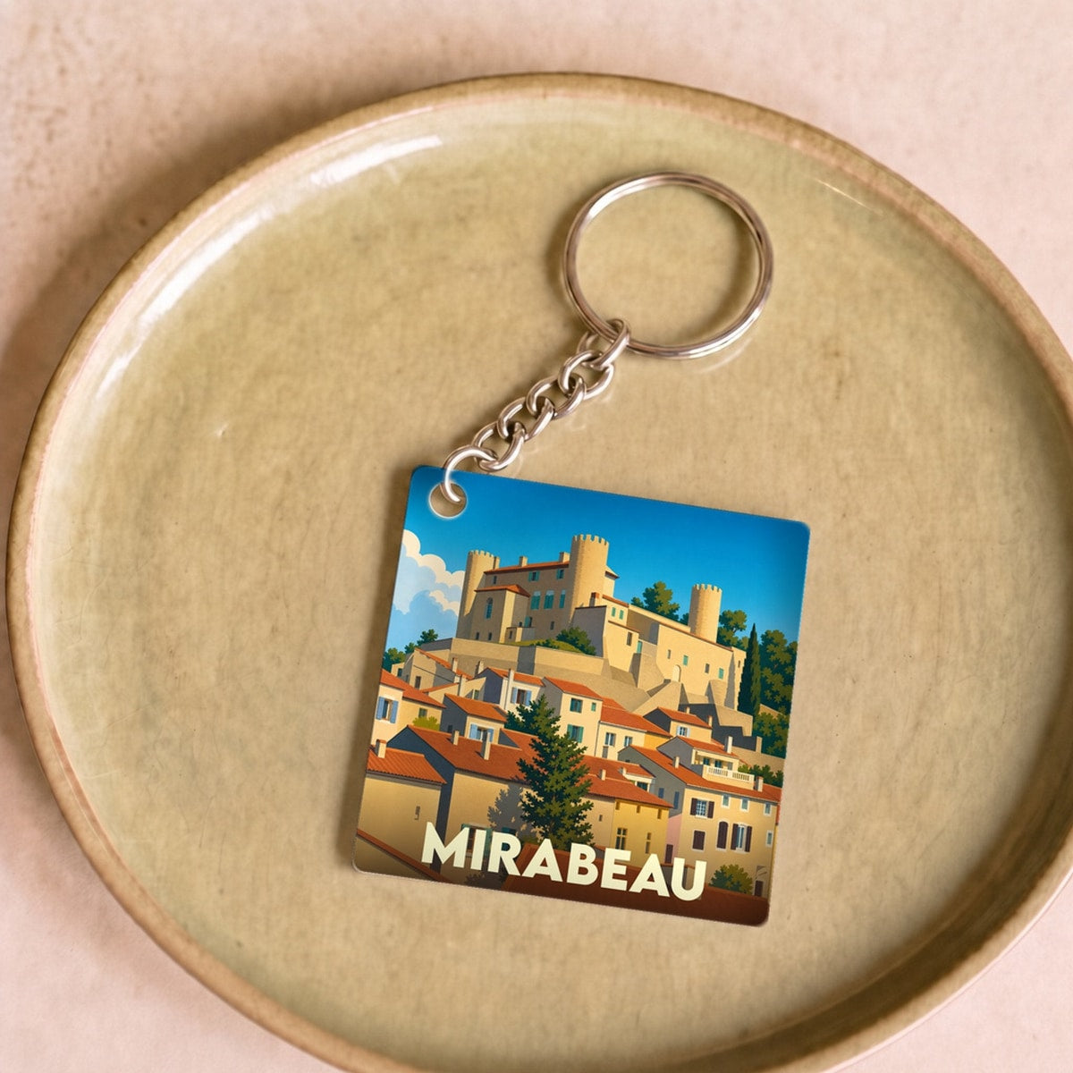 Porte-clés souvenir de la ville de Mirabeau avec une illustration stylisée d'un village provençal et son château.