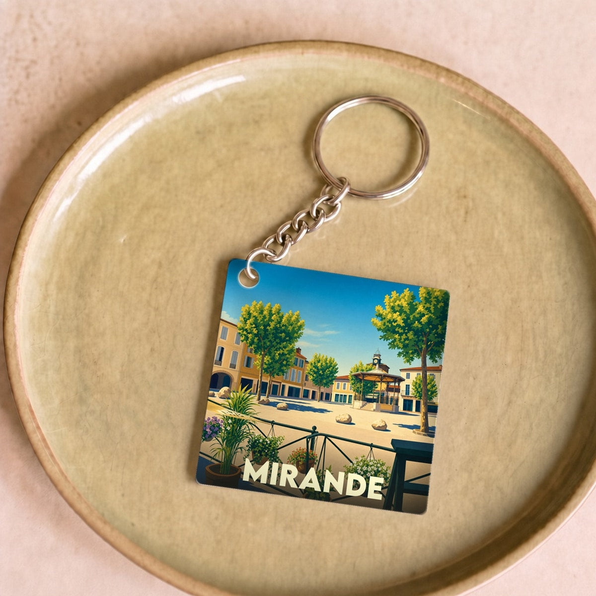 Porte-clés souvenir de la ville de Mirande avec une illustration stylisée de sa place principale.