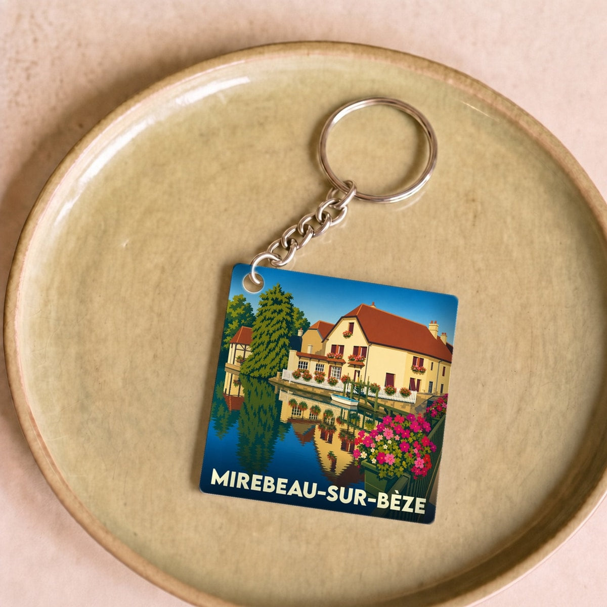 Porte-clés souvenir de la ville de Mirebeau-sur-Bèze avec une illustration stylisée d'une maison au bord de l'eau.