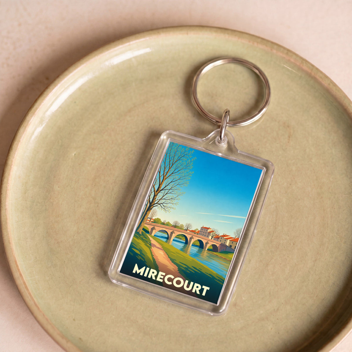 Porte-clés souvenir de la ville de Mirecourt avec une illustration stylisée d'un pont et d'une rivière.