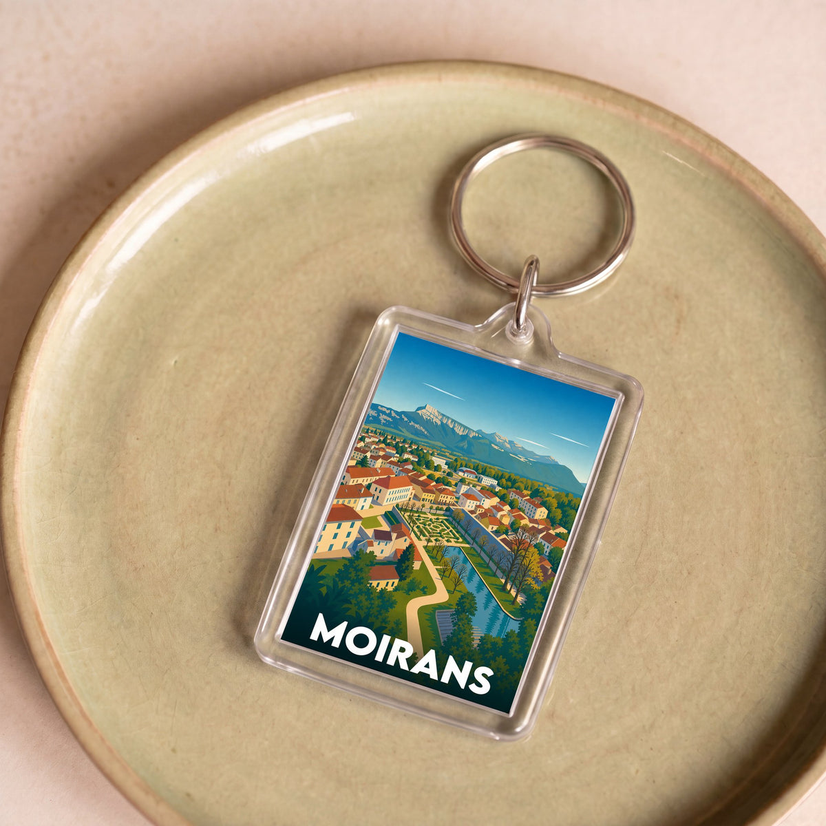 Porte-clés souvenir de la ville de Moirans avec une illustration stylisée de son paysage urbain et montagneux.