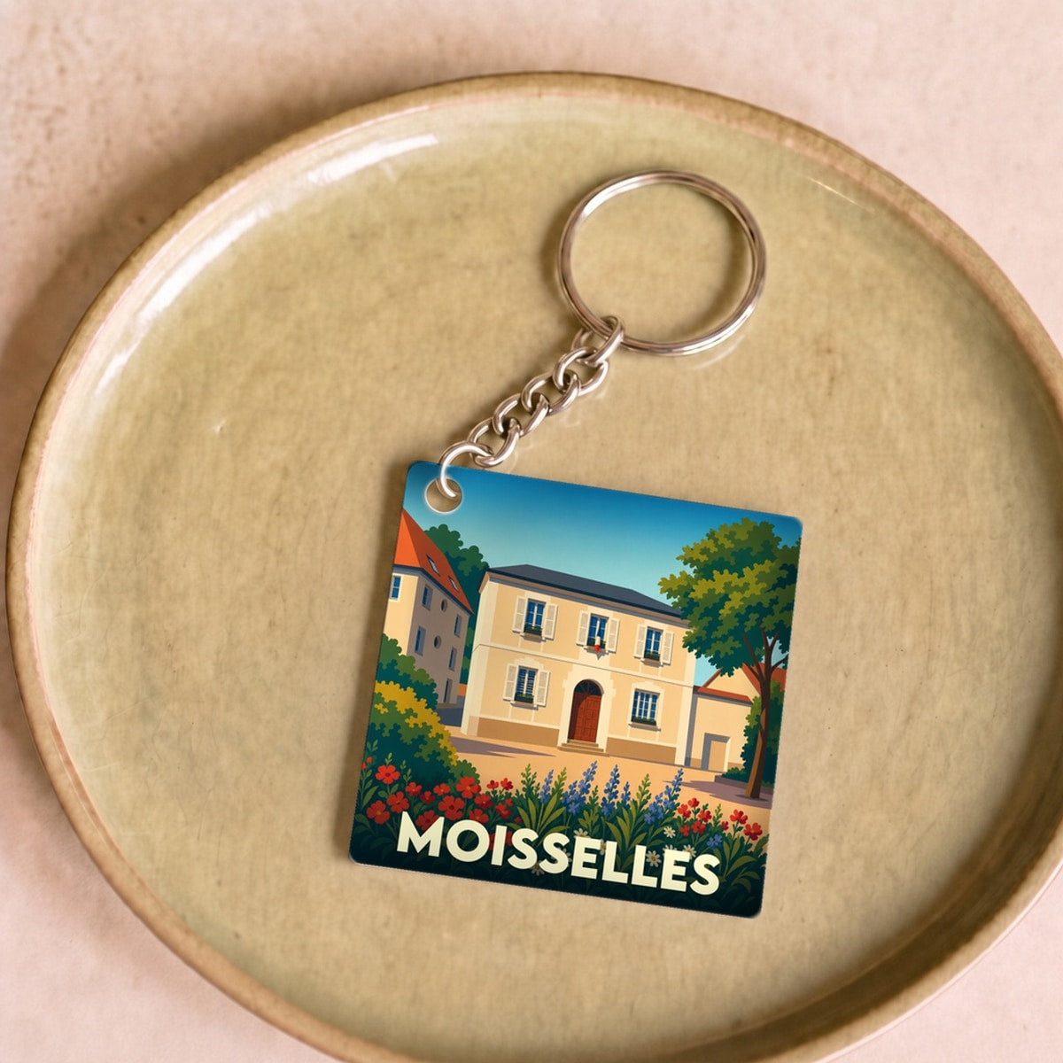 Porte-clés souvenir de la ville de Moisselles avec une illustration colorée et stylisée d'une maison fleurie.